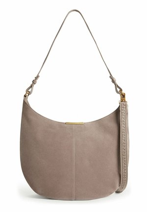 Sac à bandoulière souple en daim taupe avec quincaillerie dorée, forme courbée, sangle réglable et sangle décorative amovible avec texte embossé.