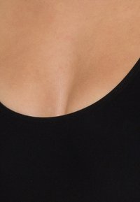 Tissu noir avec une texture lisse, présentant une large encolure dégagée. L'image montre un détail en forme de V au niveau du décolleté.