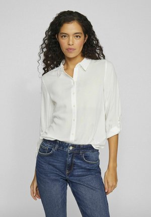 Chemise blanche à boutons avec manches longues, tissu doux, coupe décontractée et col. Associée à un jean en denim bleu foncé. Design simple.