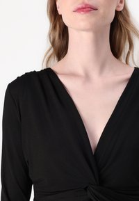 Black wrap dress with a deep V-neck, long sleeves, and a knotted waist detail. The fabric appears lightweight and smooth.