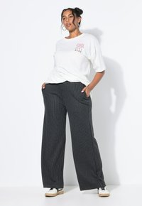 T-shirt blanche avec le texte "COOL HERE", associé à un pantalon large à rayures noires, doté de poches et d'une coupe décontractée. Baskets blanches.