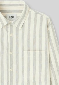 Chemise en coton avec des rayures verticales alternées crème et bleu, col boutonné et poche sur la poitrine gauche. Texture lisse, design décontracté.