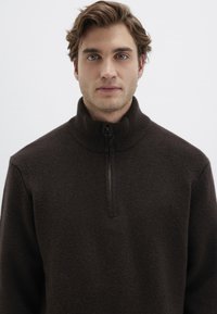 Brauner Fleece-Pullover mit hohem Kragen und halbem Reißverschluss. Verfügt über eine weiche Textur und eine lockere Passform, geeignet für lässige Kleidung.