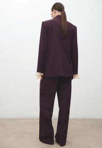 Chaqueta de traje morada a medida y pantalones a juego, con un diseño limpio, silueta estructurada y tejido texturizado. Estilo minimalista.