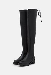 Botas negras por encima de la rodilla, fabricadas en cuero liso, con un robusto tacón cuadrado, panel trasero elástico y un mínimo detalle de costura.