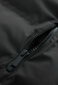 Gros plan sur une fermeture éclair noire ouverte sur un tissu noir lisse, montrant en détail les dents de la fermeture éclair et le curseur.