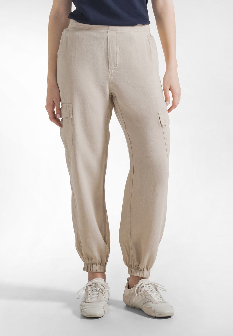 Beiget väriset cargo-housut, joissa on joustinneulos nilkan kohdalta, kaksi sivutaskua ja etuosan ompeludetaljit, valmistettu kevyestä kankaasta. Jalkineina on tennarit.