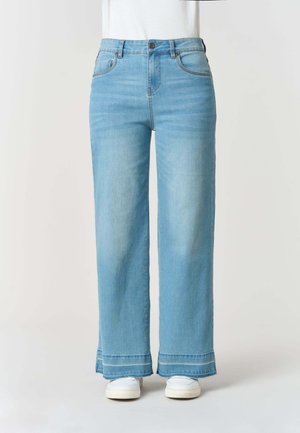 Jeans azzurri a gamba larga con vita alta, tasche frontali e orli sfrangiati, indossati con sneaker bianche e top bianco infilato.