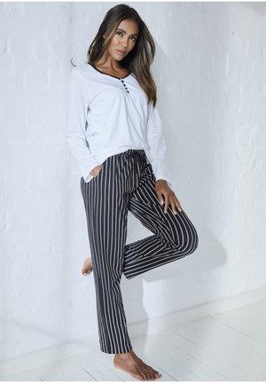 Weißes Langarmoberteil mit Knopfdetails, kombiniert mit schwarz-weiß gestreiften Loungehosen mit elastischem Bund und Seitentaschen.