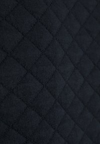 Tessuto nero trapuntato con un motivo a diamante e texture in rilievo, composto da materiale tessile morbido, ideale per capi esterni o rivestimenti.