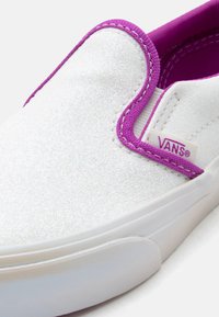 Λευκό παπούτσι Vans slip-on με υφή γκλίτερ και μωβ περίγραμμα κατά μήκος του ανοί γματος και της εσωτερικής επένδυσης, με την ετικέτα της μάρκας στη πλευρά.