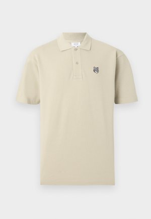 Beżowa koszulka polo z krótkim rękawem, dwoma guzikami i małym haftowanym logo głowy wilka na lewej piersi.