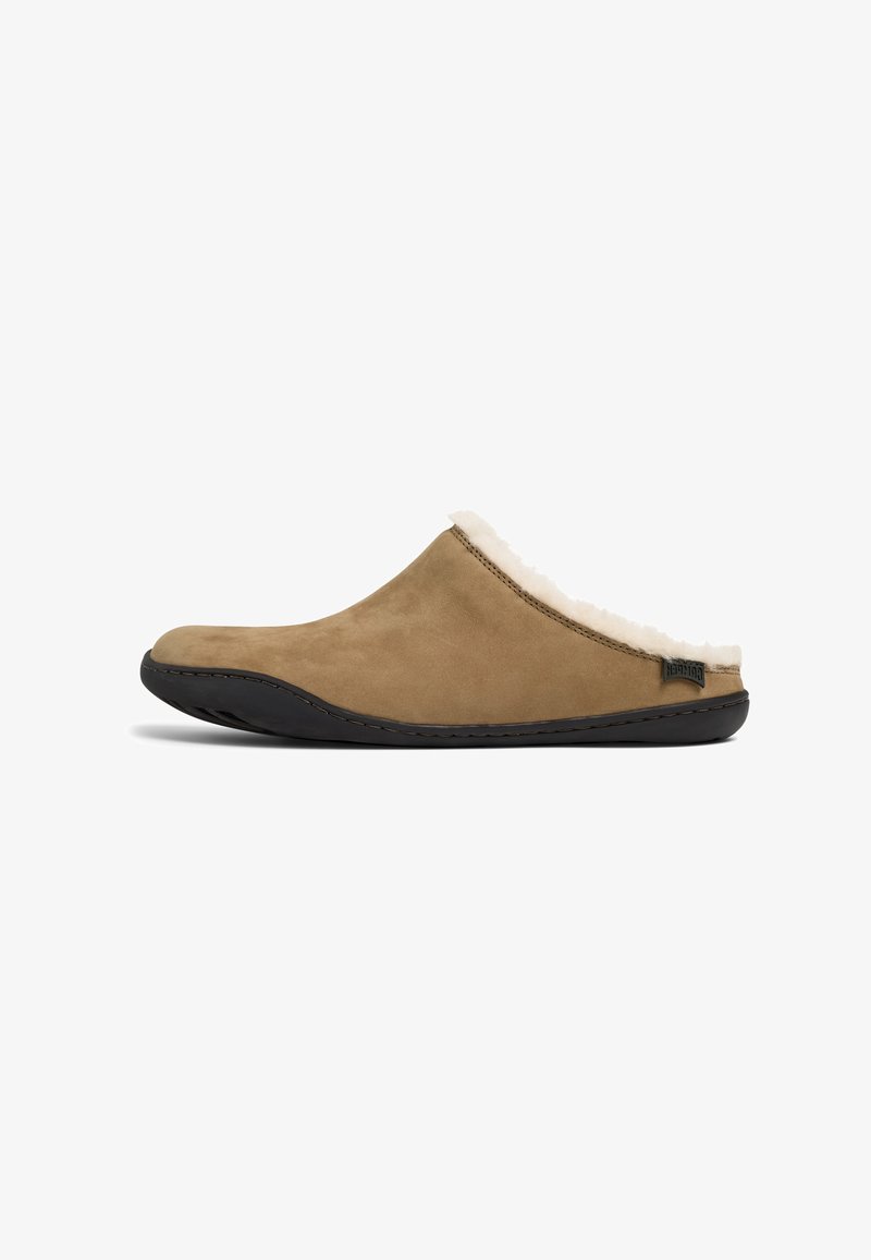 Bruine suede pantoffel met een zachte, witte bontvoering, gebogen vorm, zwarte rubberen zool en subtiele stikdetails langs de randen.