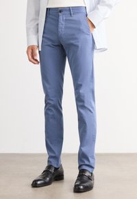 Pantalons en coton bleu clair avec une coupe slim, un devant plat et des poches latérales, associés à des chaussures en cuir noir avec un accent de boucle.