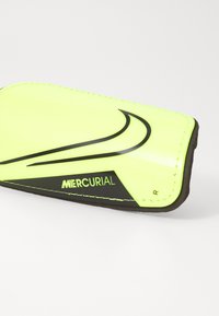 Protège-tibias jaune avec des accents noirs, présentant une surface lisse et brillante et le logo "MERCURIAL". Conçu pour un usage sur la jambe droite.