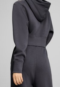 Sweat à capuche gris raccourci avec une finition texturée, doté d'une capuche et de poignets côtelés, assorti à un pantalon de jogging gris coordonné.