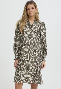 Zöld-fehér mintás ruha V-nyakkal, hosszú, fodros ujjakkal és összegyűrt mandzsettákkal, rózsaszín és sötétzöld absztrakt mintákkal díszítve.