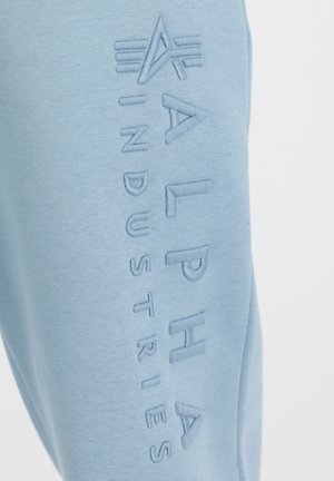 Lyseblå sweatshirt med præget "ALPHA INDUSTRIES" tekst på venstre side. Blødt stof med en hyggelig tekstur.