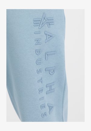 Világoskék pulóver, az "ALPHA INDUSTRIES" címkével, amely kiemelkedik a bal oldalon. Puha anyagú, kényelmes textúrával.