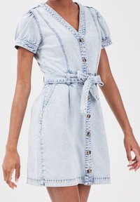Light blue denim dress with short puff sleeves, a V-neck, front buttons, and a fabric belt at the waist. Distressed texture and stitching details.
