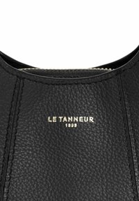 Superficie in pelle nera testurizzata con testo in rilievo dorato "LE TANNEUR 1898" centrato vicino al bordo superiore.
