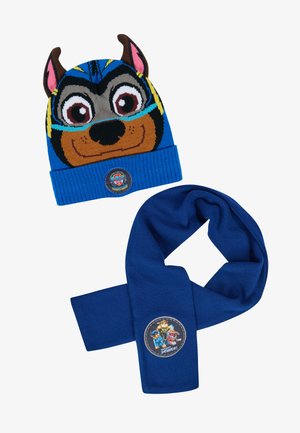 Blauwe gebreide muts met dierengezicht, voorzien van bruine oren en blauwe gestreepte details. Vergezeld van een effen blauwe sjaal met een karakterapplicatie.