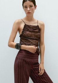 Brun, texturerad camisole med volanger, matchad med mörk vinröd, randig hög midja-byxa. Svart armband på handleden.