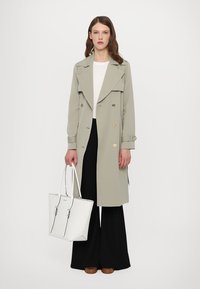 Light gray double-breasted trench coat with large lapels, paired with a white top and black wide-leg trousers. White tote bag with hardware accents.