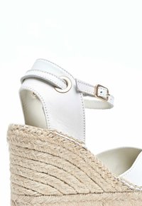 Sandalia de cuña de cuero blanco con tacón de yute trenzado, que cuenta con una correa ajustable en el tobillo y un acabado suave y texturizado.