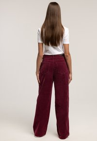 Bordowe szerokie spodnie sztruksowe o teksturowanej powierzchni, z tylnymi kieszeniami i wysokim stanem, zestawione z białym t-shirtem.