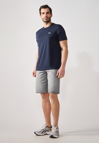 Navy short-sleeve t-shirt featuring a small logo on the chest, paired with gray shorts. Model wears gray and white athletic shoes.