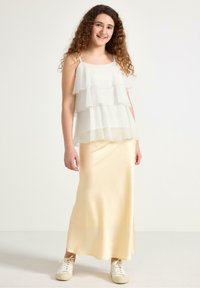 Top in chiffon bianco a strati con spalline regolabili, abbinato a una gonna maxi in satin giallo pallido e sneakers bianche. Texture liscia e design fluido.