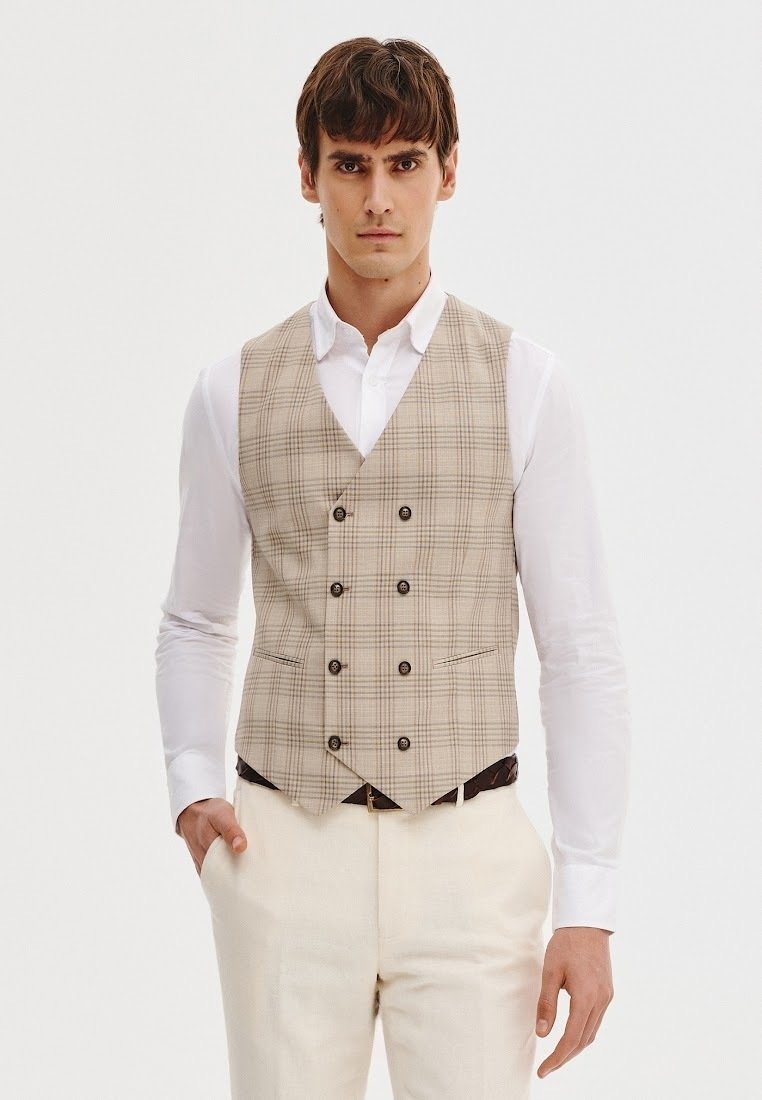 Beżowa kamizelka w kratę z podwójnym zapięciem, posiadająca pięć guzików, dwie przednie kieszenie oraz fakturowany materiał, zestawiona z białą koszulą.