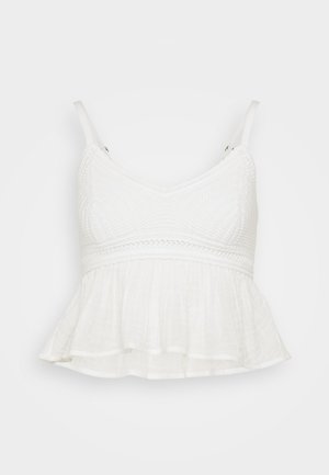 Top corto blanco hecho de una tela texturizada, con un corpete ajustado, tirantes ajustables y un dobladillo acampanado con volantes.