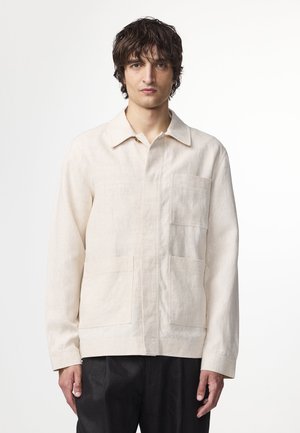 Chemise en lin beige clair avec un col, fermeture à boutons sur le devant et deux grandes poches à soufflet. Elle possède des manches longues et une coupe décontractée.