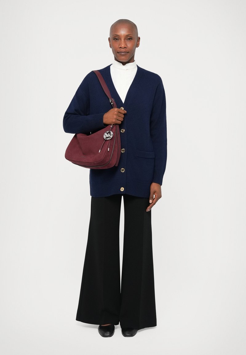 Mornarski pleteni kardigan s gumbima, uparen s bijelim topom s visokim ovratnikom. Crne hlače širokih nogavica i bordo torba s srebrnim akcentima.