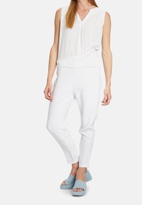 Bílý bezrukávový top s výstřihem do V, zkombinovaný s bílými zúženými kalhotami a světlemodrými semišovými sandály. Jednoduchý design, jemná textura a neutrální barva.