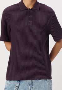 Polokošile s krátkým rukávem z tmavě fialové žebrované látky. Má límec, tři knoflíky a volný střih. Texturovaný povrch s olemovanými okraji.