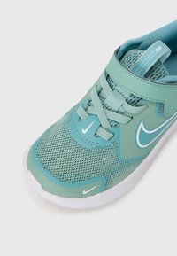 Chaussure de sport turquoise clair avec tige en maille, détails texturés, fermeture à lacets et accents blancs, y compris le logo Nike.