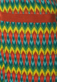 Vícebarevná pletená textilie s geometrickým vzorem v červené, zelené, žluté a modré. Obsahuje solidní hnědý vodorovný pruh.