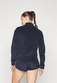 Veste en polaire bleu marine avec un col haut et une taille élastique, accompagnée de shorts assortis avec des garnitures blanches. Texture douce.