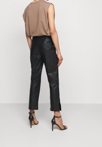 Brun ärmlös topp matchad med svarta läderbyxor med smal passform och ankeldelar, bärs med svarta stilettklackar.