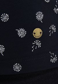 Laivastonsininen kangas, jossa on valkoisia kukkakuvioita, ja kultainen Esprit-logo, joka on kiinnitetty mustalla langalla, korostaen tekstuuria ja ompelutietoja.