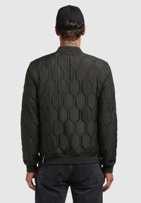 Tmavozelená prešívaná bomber bunda s hexagonálnym vzorom, rebrovanými manžetami a spodným lemom, a jednoduchým, čistým dizajnom. Žiadne viditeľné logo.