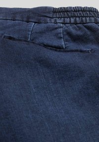 Gros plan sur un tissu bleu marine de pantalons avec une ceinture élastique et une texture lisse, présentant un léger éclat et des coutures nettes.