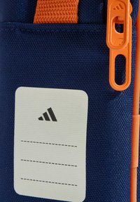 Niebieski materiałowy uchwyt z pomarańczowym suwakiem i paskiem. Zawiera białą etykietę do identyfikacji z czarnymi liniami do pisania.