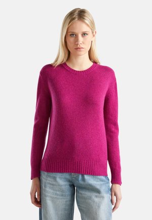 Fuchsiastrickpullover mit rundem Halsausschnitt, gerippten Bündchen und Saum. Weiche Textur, lockere Passform, präsentiert mit hellblauen Jeans.
