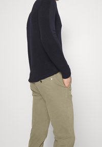 Marinblå stickad tröja med ribbad textur, ihopparad med ljus khakifärgade chinos med sidofickor och knappstängning. Avslappnad och åtsittande design.