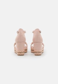 Sandalias de tacón alto de ante rosa con plataforma de yute trenzado y tira en el tobillo. Diseño de espalda abierta con múltiples tiras sobre el pie.