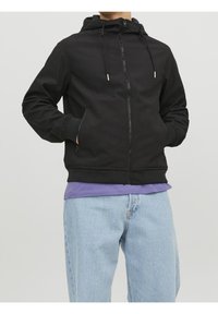 Czarna bluza z kapturem zapinana na zamek, z regulowanym sznurkiem w kapturze, bocznymi kieszeniami i ściągaczami na rękawach. Noszona na fioletowej koszuli, w połączeniu z jasnoniebieskimi dżinsami.